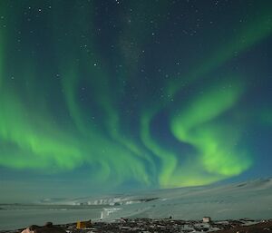 A bright green aurora lights up a plateau and frozen bay of sea ice