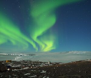 A bright green aurora swirls over an ice covered plateau