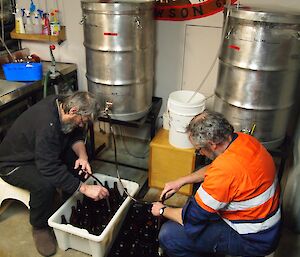 Two men fills bottles of beer from a keg.