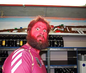 A man with a red painted face stares at the camera.