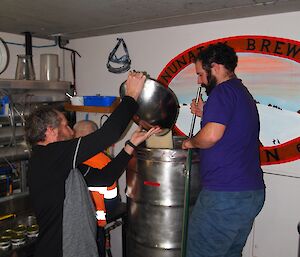 A man adds a bowl of sugar to a beer keg.