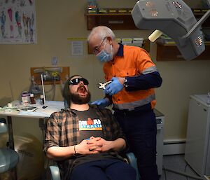 A dentist is looking into the mouth of a man.
