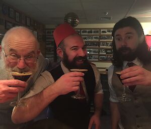 Three men standing in a bar drinking cocktails.