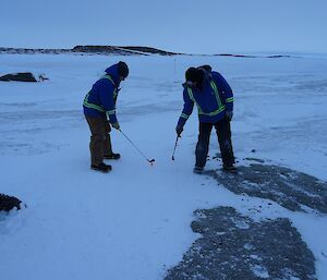 Two men stand on sea ice playing golf.