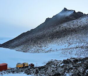 A red hut, yellow Hägglunds vehicle and a mountain peak.