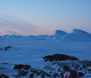 A frozen landscape with blue icebergs and a pink sky