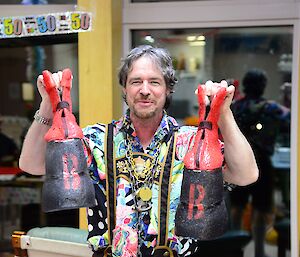 A man holds up red and black platform boots.