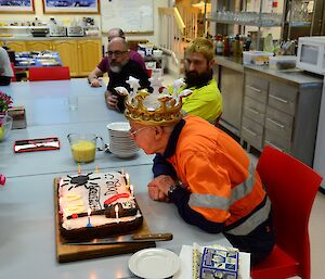 A man in a crown blows out birthday candles.