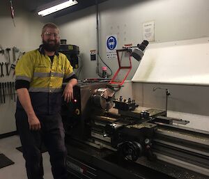 A man stands in front of a lathe machine.