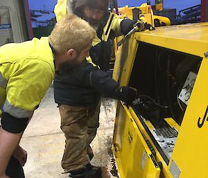 Two men stand in front of a yellow portable air compressor