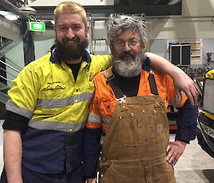 Two men stand side by side in work clothing.