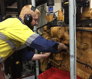 A man wearing headphones is working on a yellow engine