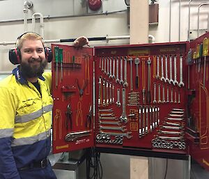 A man stands in front of an open tool cabinet.