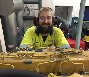 A man wearing head phones crouches in front of an engine