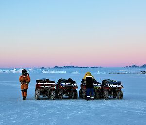 Two men and four quad bikes are lined up on the blue sea ice