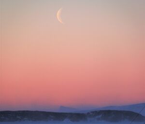 The sunrise is apricot pink in colour over snow.