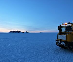 A Hägglunds vehicle is parked on the ice with a mountain range in the background