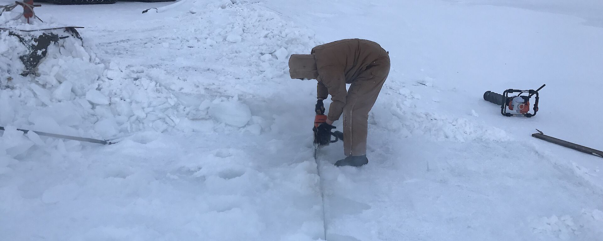 A man is cutting into the ice with a chainsaw.
