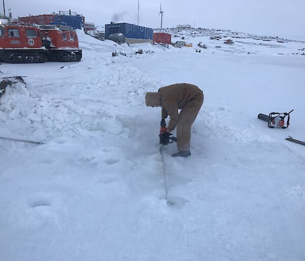 A man is cutting into the ice with a chainsaw.