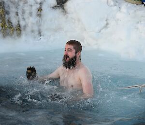 A man with a beard is jumping out of the water with a glove on