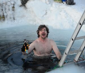 A man descends a ladder into cold water with his mouth wide open