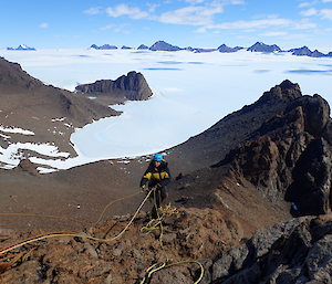 A woman descends a rocky mountain with ropes.