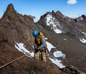 A man wearing a blue helmet descends a rocky mountain peak