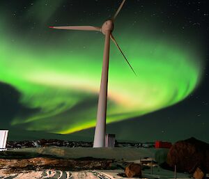 A flourescent green and white aurora behind a tall wind turbine