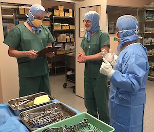 Three men stand in a theatre in hospital scrubs.