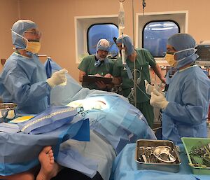 Four men attend to a covered over patient on a hospital theatre bed.