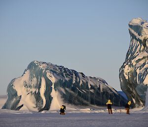 Three expedtioners stand in front of a jade iceberg.