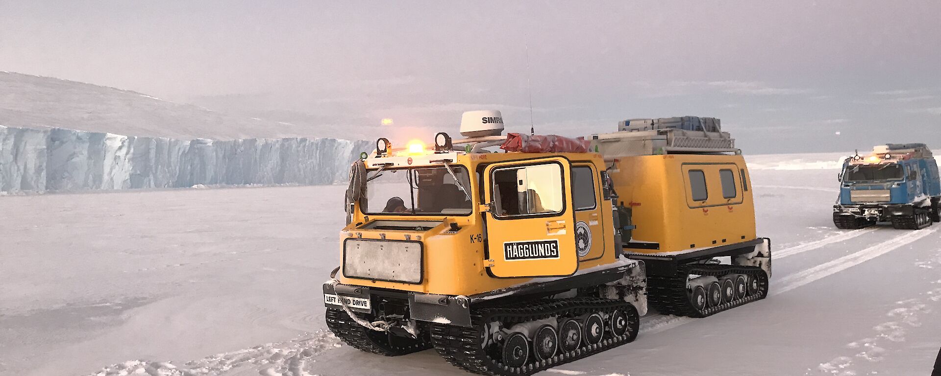 A yellow Hägg parked in front of an ice cliff edge.