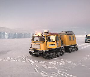 A yellow Hägg parked in front of an ice cliff edge.