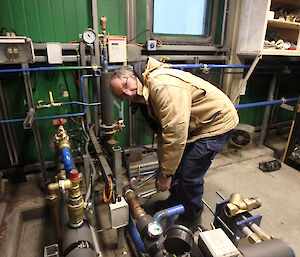 A man is leaning over a set of pipes checking them.