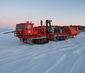 A big red truck on tracks tows an orange caravan on skis