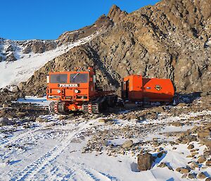 A red truck reverse parks an orange caravan in front of a mountain