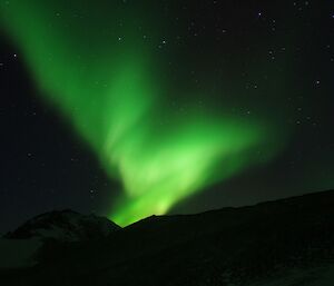 A green aurora spirals above a mountain range.
