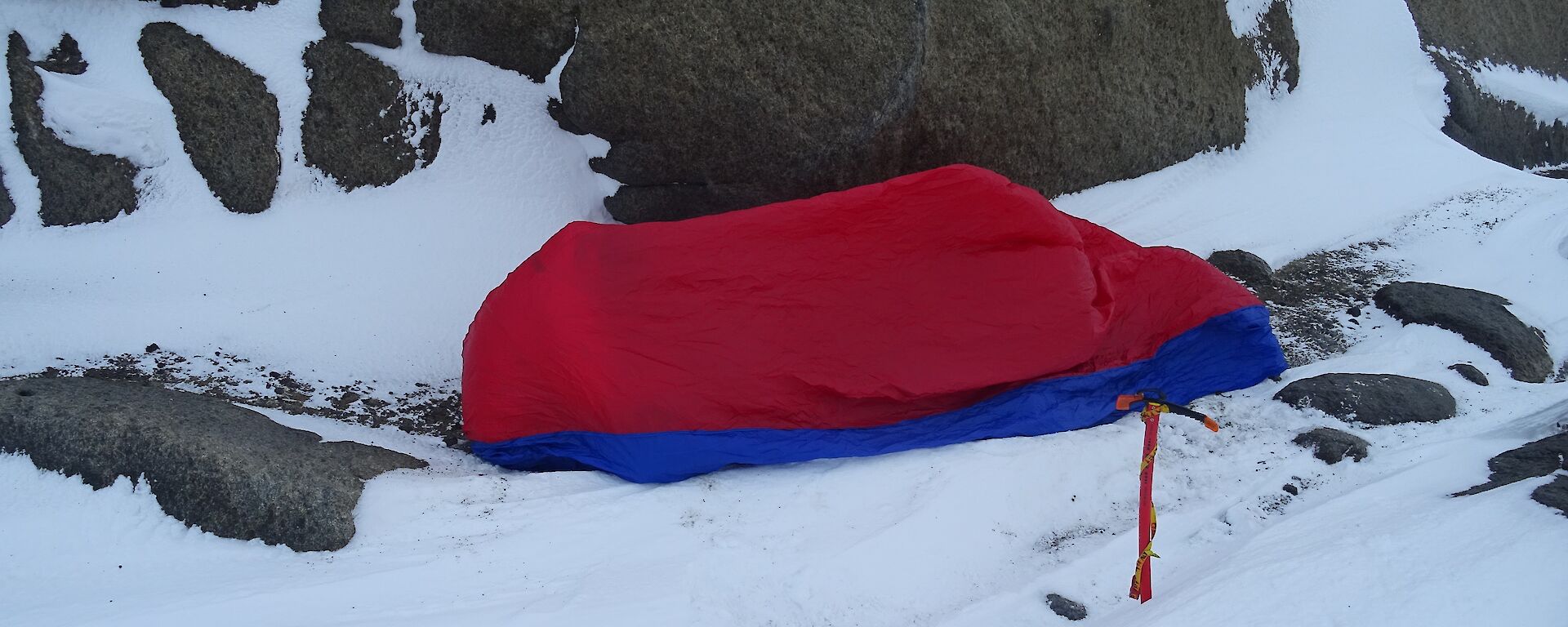 A red plastic bivvy bag next to a rocky embankment