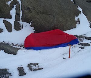 A red plastic bivvy bag next to a rocky embankment