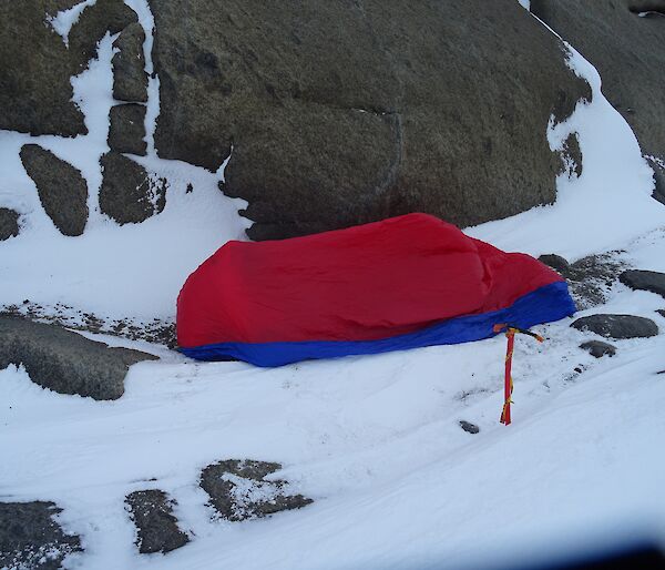 A red plastic bivvy bag next to a rocky embankment