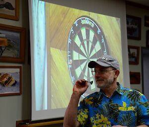 A man in a Hawaiian shirt aiming to throw a dart.