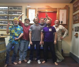 Six men stand in front of a darts board.