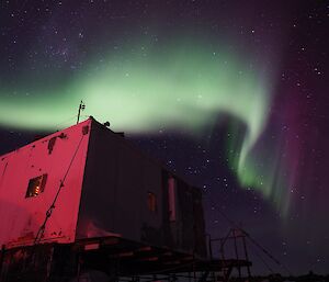 A white, green and violet aurora above a red tinged building