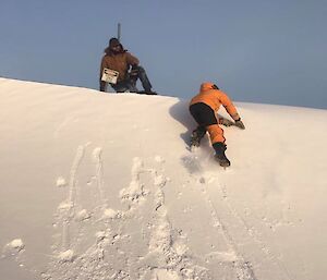 Two men climb up an embankment of snow.