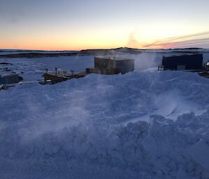 An embankment of snow overlooking buildings with pink sunrise.