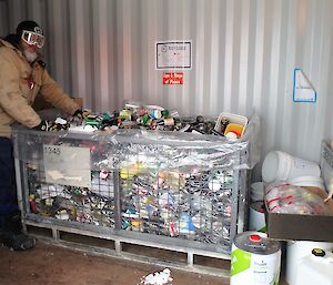 A man stands in front of a cage pallet full of recycled items.