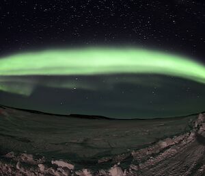 A light green band of light curves across a harbour of frozen sea ice