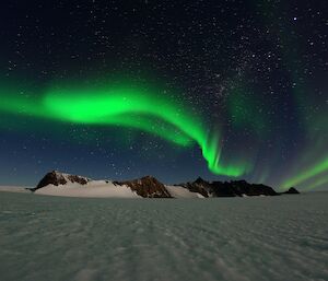 A bright green swirl of light appears over a mountain range and frozen plateau