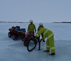 Three men set up a mobile pump on the sea ice to drain water from a hole in the ice