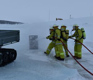 Four people in fire fighting gear hold fire hoses on the sea ice.